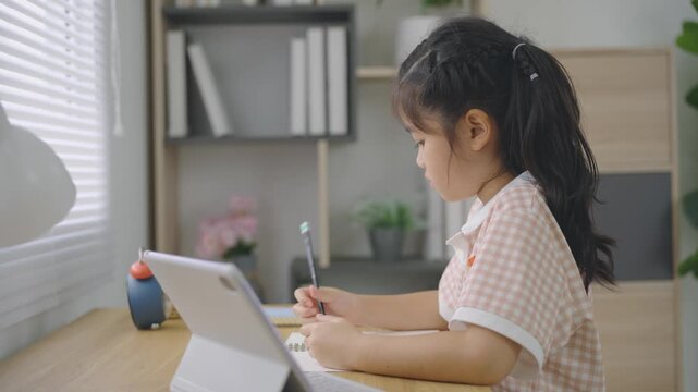 Young girl sitting at desk using tablet for learning and drawing with stylus pen in bright cozy room by window daylight