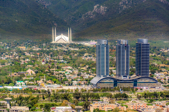 Aerial view of Faisal Masjid and modern skyscrapers surrounded by lush greenery and the Margalla Hills in Islamabad, Islamabad Capital Ter, Pakistan.
