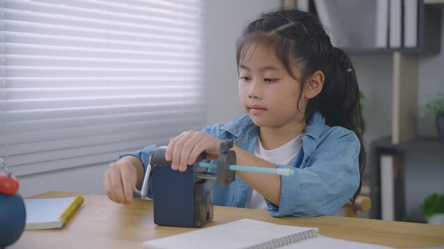 Young focused girl sharpening pencil with manual sharpener while sitting at desk in bright modern room