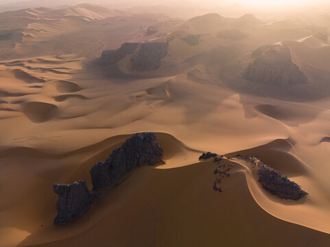 Aerial view of Sahara desert with golden sand dunes and rocky outcrops in Algeria.
