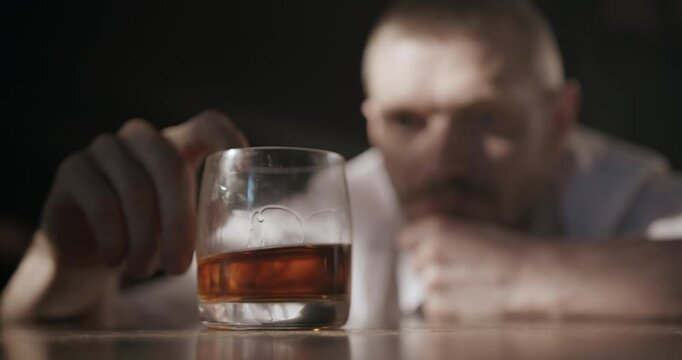Close-up of a glass of alcohol as a troubled man reaches toward it but ultimately decides not to drink.