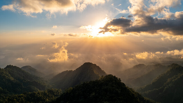 Aerial view of lush green mountains at sunrise with golden light filtering through clouds over the landscape in Bajawa, Nusa Tenggara Timur, Indonesia.