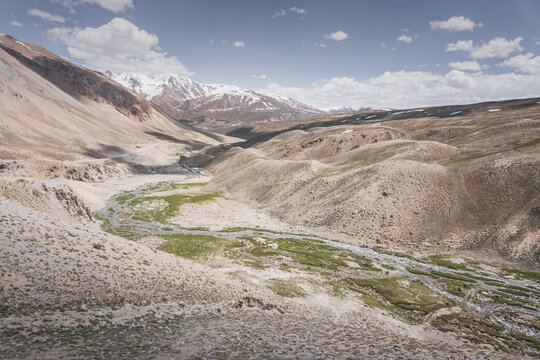 Landscape in the Pamir Mountains with a river valley below and mountain slopes with peaks in the background, mountain range with snow and glaciers in the Tien Shan Mountains