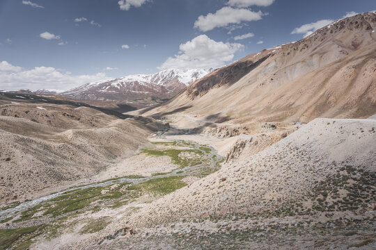 Landscape in the Pamir Mountains with a river valley below and mountain slopes with peaks in the background, mountain range with snow and glaciers in the Tien Shan Mountains
