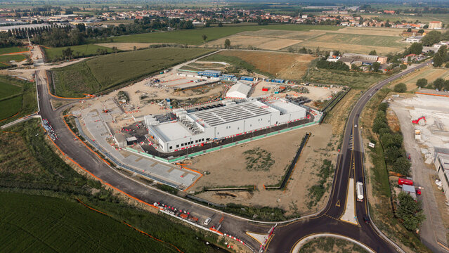 Aerial view of the BYES MIL08 data center construction site, featuring a large industrial building, surrounding access roads, and rural landscape in Siziano, Lombardia, Italy.