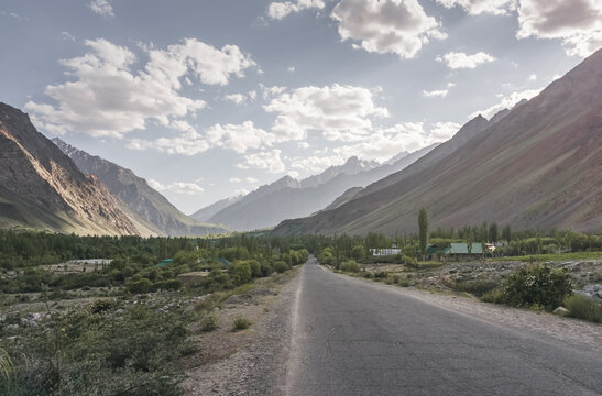 Asphalt road of the Pamir Highway among rocky peaks and sparse vegetation. Landscape in the Tien Shan Mountains in the evening