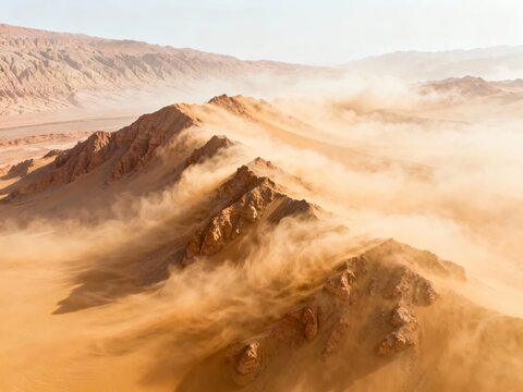 Aerial view of desert mountains engulfed in sandstorm with swirling dust and rugged terrain