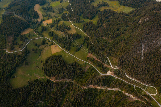 Aerial view of the mountainous landscape near Fiss, featuring winding roads, dense pine forests, green meadows, and power lines cutting across the terrain in Fiss, Tyrol, Austria.