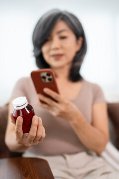 Asian woman holding bottle of food supplement or medicine using computer typing searching online prescription  pill bottle  information online.