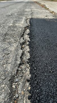 A stark visual contrast between aged weathered asphalt and fresh dark bitumen patch