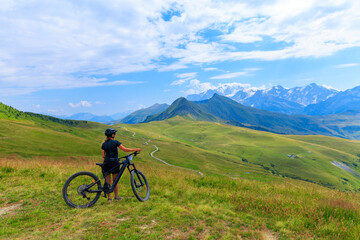 Fototapeta premium Woman with electric mountain bike on alpine ridge looking at snowcapped mountains, mount blanc in France