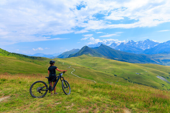 Woman with electric mountain bike on alpine ridge looking at snowcapped mountains, mount blanc in France