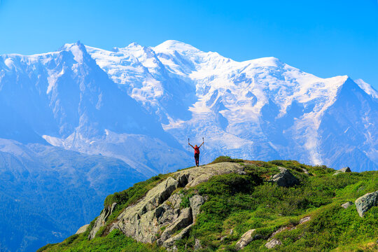Happy silhouette of Hiker standing on mountain ridge raising arms in success against snowcapped Mont Blanc peak, Alps in France