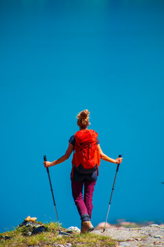 Rear view of female hiker with red backpack looking at turquoise blue mountain lake in Swizterland, Alps, Emosson