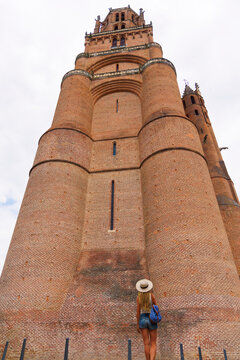 Low angle view of female tourist looking up at massive brick bell tower of Albi cathedral in France