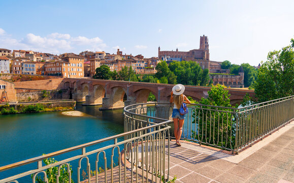 Rear view of female tourist with hat standing on bridge looking at Albi cathedral and river in France