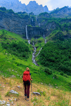 Rear view of female hiker with red backpack walking towards dramatic mountain waterfalls, Alps, Sixt Fer a Cheval circus France, Le bout du Monde