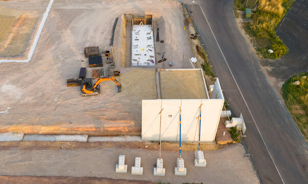 Aerial view of a construction site for a new supermarket featuring a concrete foundation, a standing wall with braces, and an excavator in Trier-Saarburg, Rhineland-Palatinate, Germany.