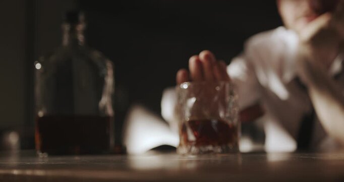 Close-up of a man moving a glass of liquor away from himself, suggesting a decision to stop drinking.
