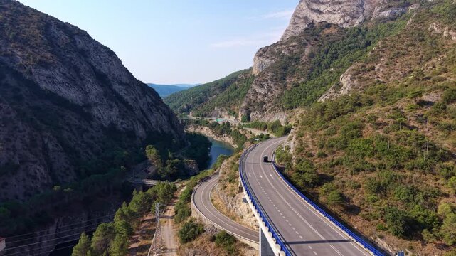 Highway curves through a mountain gorge near Oliana Dam on the Segre River, Lleida, Spain, with lush green slopes, rocky cliffs and a reservoir visible below