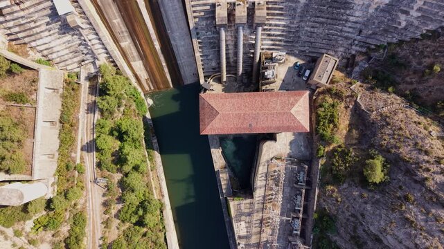 Top-down view of Oliana dam on the Segre River in Lleida, Spain, showing concrete spillway steps, hydroelectric powerhouse building and green water channel