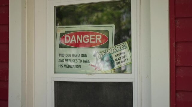Static shot of a humorous beware of dog sign displayed in the window of an old farmhouse in a rural setting