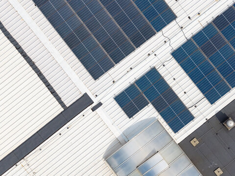Aerial view of a modern factory warehouse roof featuring rows of solar panels, metal roofing sheets, and skylights in Poland.