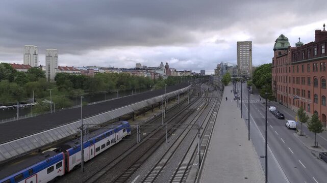 Timelapse of Stockholm&rsquo;s Torsgatan with trains, cars, pedestrian traffic and historic buildings under cloudy skies, highlighting the city&rsquo;s layered transport network.