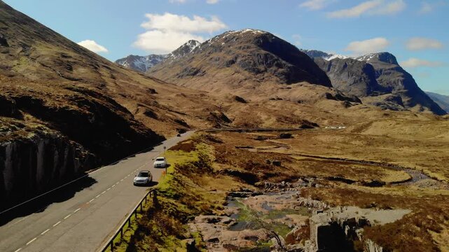 Crane shot rises from Glencoe burn to reveal Three Sisters mountains beyond.