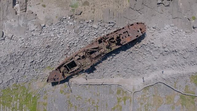 Rust-eaten Plassey cargo ship rests on bare rock slabs and boulders as the drone hovers high above the Aran Island coast.