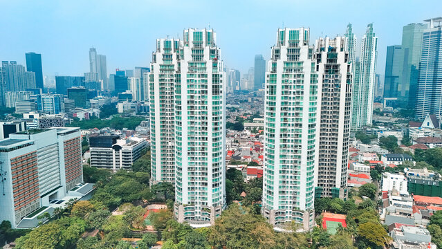 Aerial view of modern high-rise residential towers surrounded by lush greenery and the dense urban skyline of Jakarta, Indonesia.