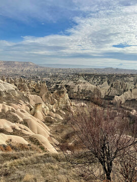 Panoramic view of Cappadocia landscape with fairy chimneys and rock formations under a cloudy blue sky in Goreme, Turkey.