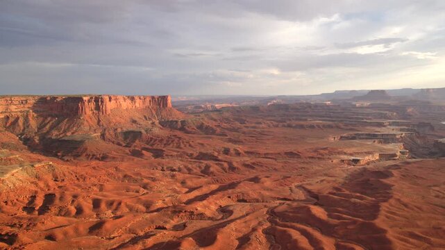 Breathtaking panoramic view of Canyonlands National Park in Utah during golden hour. Vast red rock desert terrain with dramatic mesas and buttes stretching to the horizon under cloudy skies.