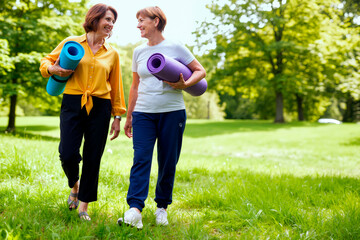 Obraz premium Caucasian middle aged women walking through park carrying yoga mats and talking, promoting active lifestyle and friendship. Useful for wellness, fitness, healthy aging marketing