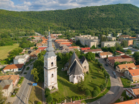 Aerial view of the historic Reformed Church with its tall bell tower, surrounded by green lawns, town rooftops, and rolling hills in the background in Plesivec, Kosice Region, Slovakia.
