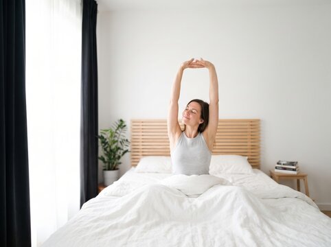 Young woman stretching arms in bed after waking up in the morning, feeling refreshed and ready for the day.