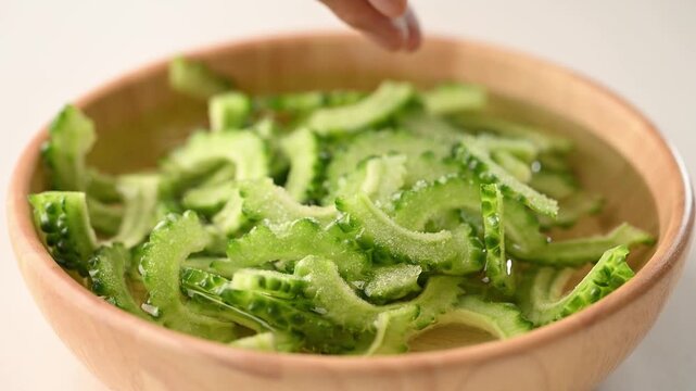 Woman's hand pouring salt powder into sliced bitter gourd soaked in water to reduce bitterness