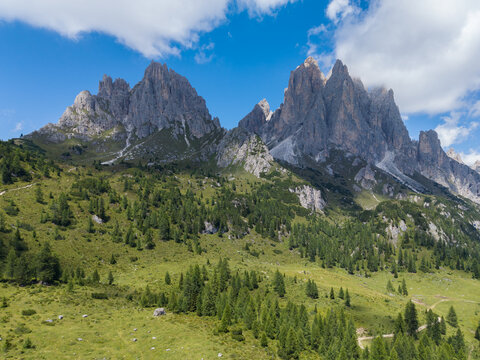Aerial view of the rugged peaks of the Cadini di Misurina mountain group with lush green alpine meadows and coniferous forests in the foreground near Auronzo di Cadore, Veneto, Italy.