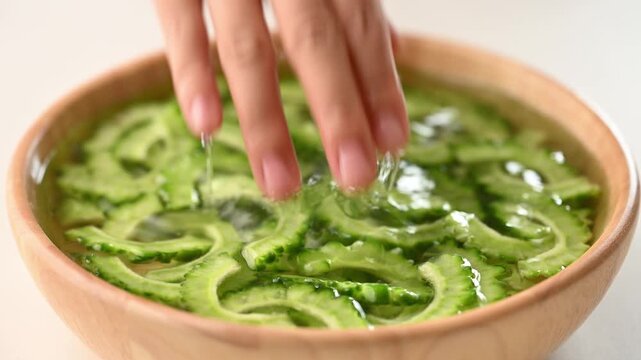 Woman hands soaking a sliced bitter gourd with salt and water in a wooden bowl to reduce bitterness