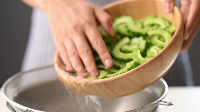 Woman hands draining excess saltwater from a bowl with sliced bitter gourd