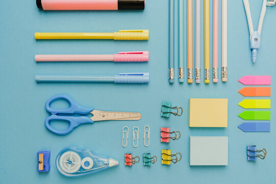 Collection of colorful stationery items arranged neatly on a blue background, including pens, pencils, scissors, and paper clips.