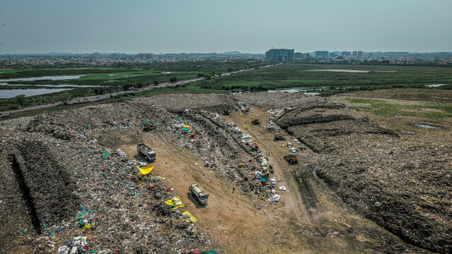 Trucks working across an open waste dump yard with the city on the horizon