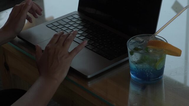 Close view of female freelancer working on laptop with notebook, phone and drink on cafe table, showing a productive remote work setup in a tropical destination