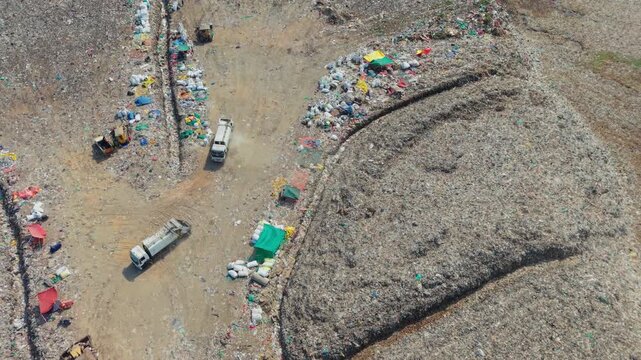 Two garbage trucks reversing to dump waste at a dump yard