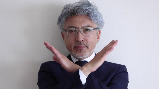 腕でバツ印を作り拒否・禁止の意思を示すスーツ姿のシニア男性