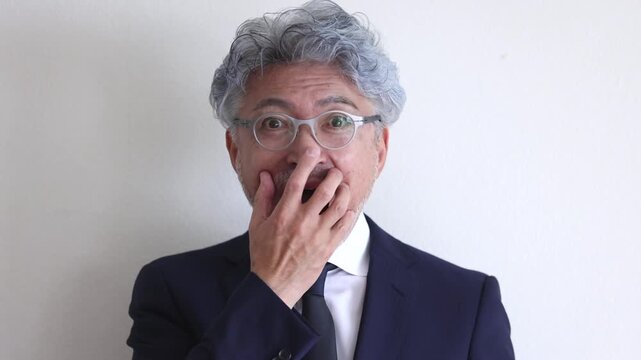 驚いて口元に手を当てるスーツ姿のシニア男性ビジネスマン