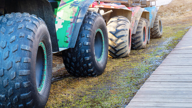 Large vehicle tires parked on a dirt area next to a wooden path in the countryside