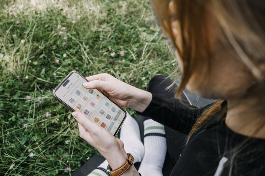 Woman in athletic wear sits on yoga mat in grass holding smartphone displaying symptom log screen. Symptom tracker app, daily mood log, health symptom diary, Mood tracking interface, wellness journal