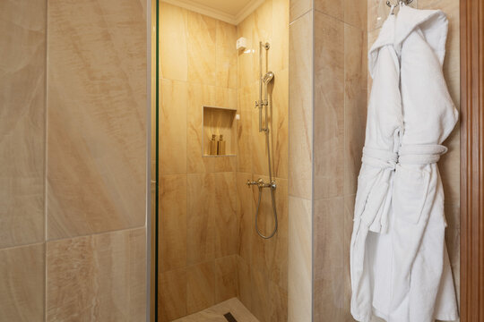 Modern luxury walk in shower with beige tile walls and bathrobe