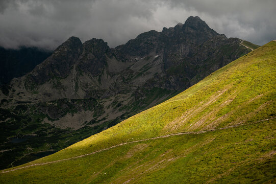 Sunlight on a green hill before stormy mountains